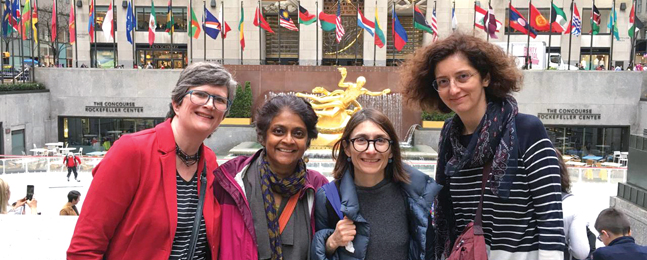 Four smiling women stand outside Rockefeller Center in New York City